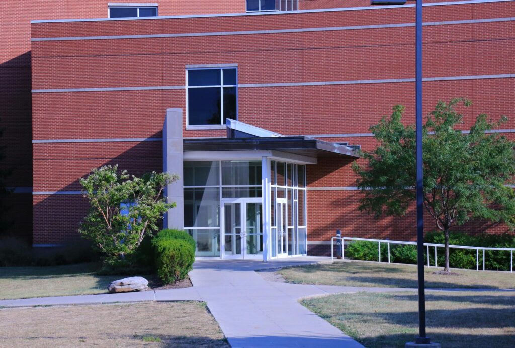 A contemporary brick building exterior with a glass door, garden, and pathway in daylight.