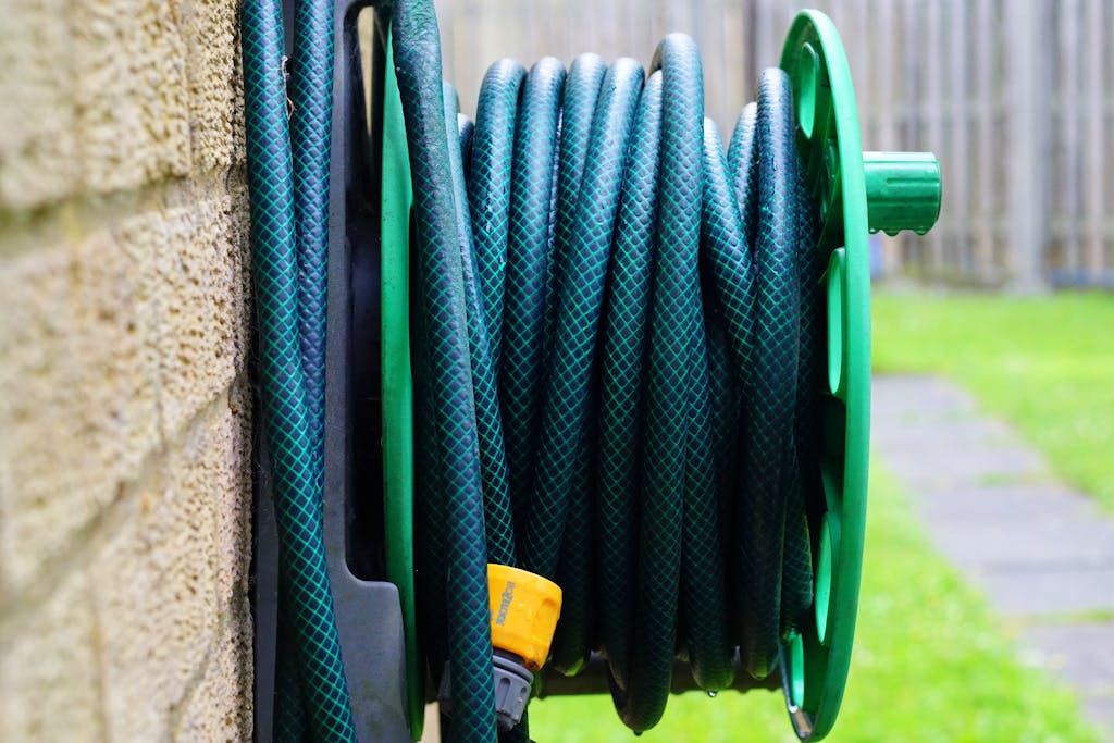 A neatly coiled garden hose on a wall-mounted reel against a brick wall.